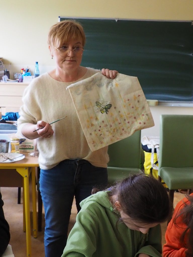 Osoba prowadząca zajęcia prezentuje ręcznie pomalowaną bawełnianą torbę
