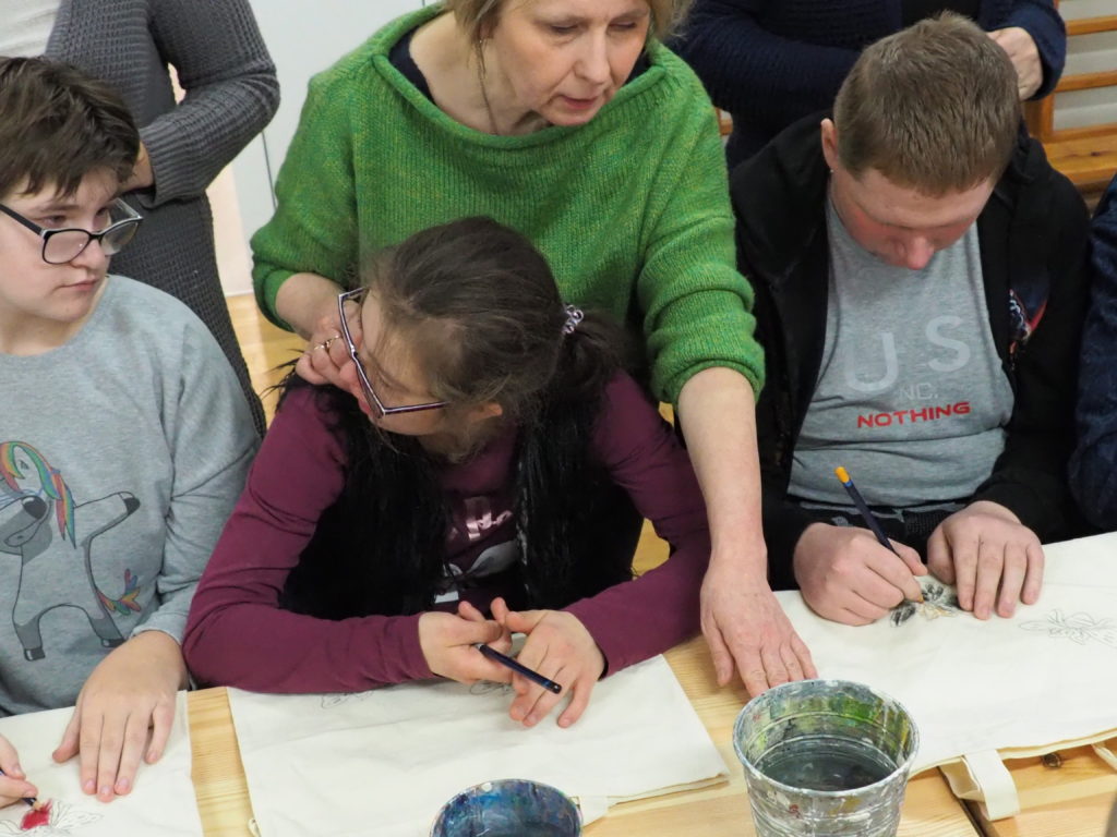 Trzech wychowanków wraz z nauczycielką malują farbami swoje torby